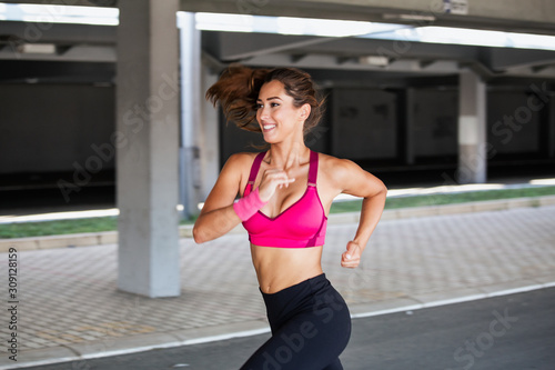 Young woman with fit body jogging and running against grey background. Female model in sportswear exercising outdoors.