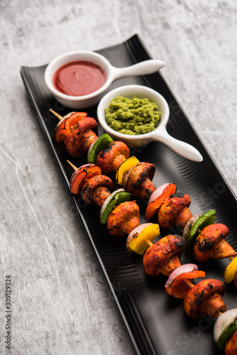 Barbecue or tandoori Mushroom Tikka, served in a plate with green chutney and ketchup. selective focus
