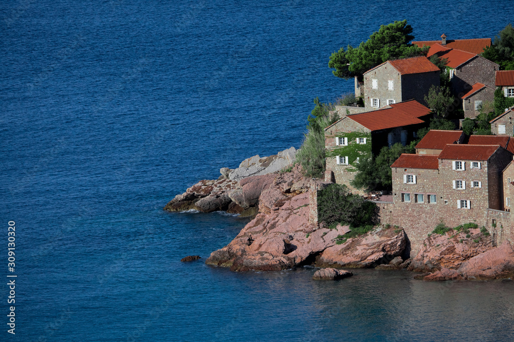 Cute fishing village.  houses with a tiled roof and green trees by the blue sea. happiness in relaxation in warm countries. Sveti Stefan
