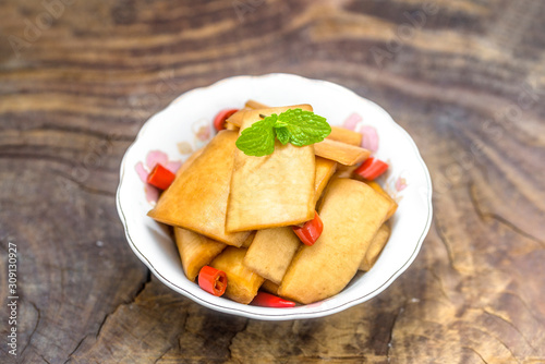 A bowl of sour radish slices sits on an old wooden board, decorated with a mint leaf.