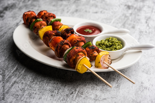 Barbecue or tandoori Mushroom Tikka, served in a plate with green chutney and ketchup. selective focus