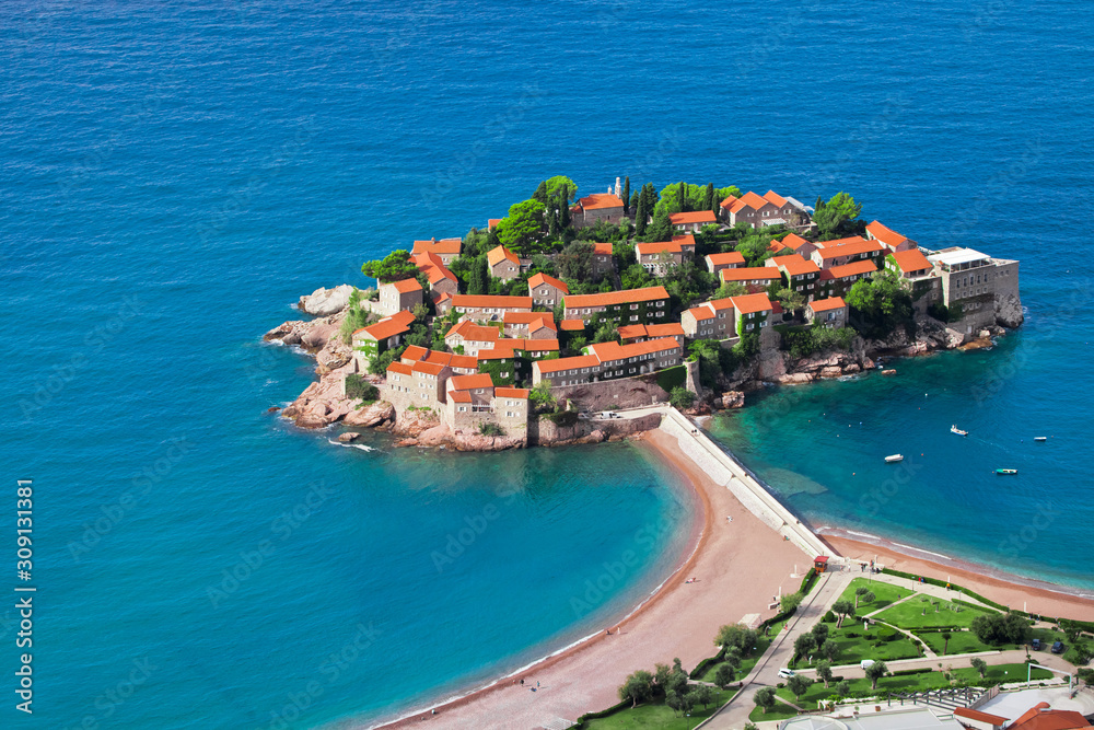  houses with a tiled roof and green trees by the blue sea. happiness in relaxation in warm countries. Sveti Stefan