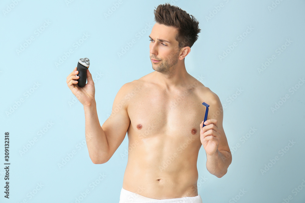 Fototapeta premium Handsome young man with razor and electric shaver on color background