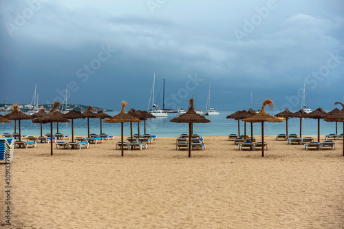 wide sandy beach with sun loungers and straw umbrellas on the background of the blue sea and white yachts in the Spanish resort of Magaluf