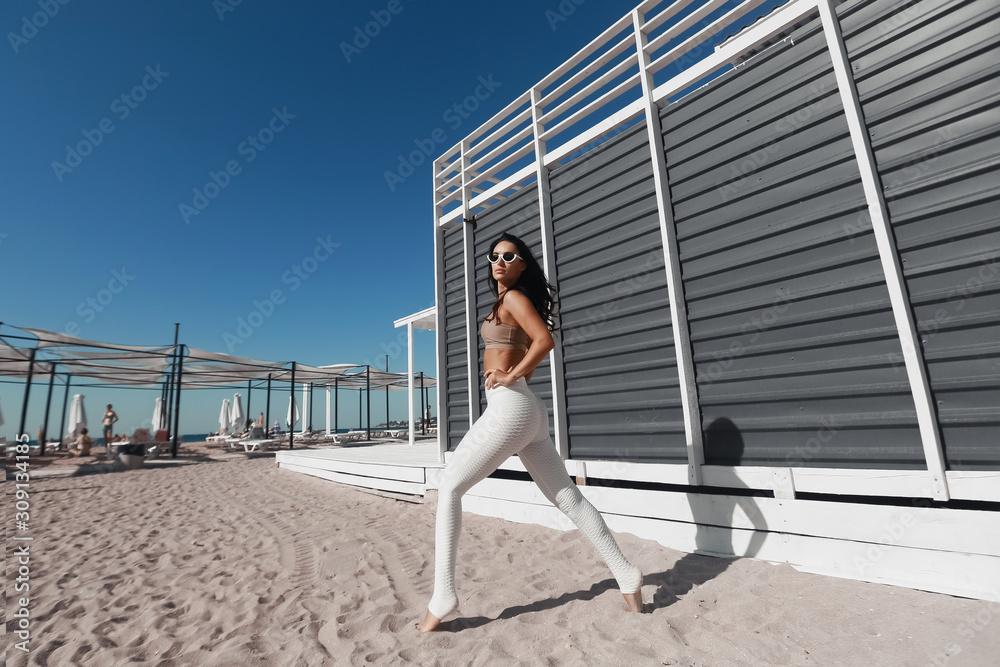 Picture of young beautiful fitness girl makes sport exercises with sea coast on background.