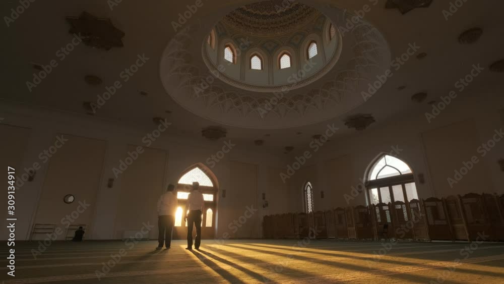 Two young men pray in a mosque. Sunset light falls through a window opening Two young men pray in a mosque. Sunset light falls through a window opening