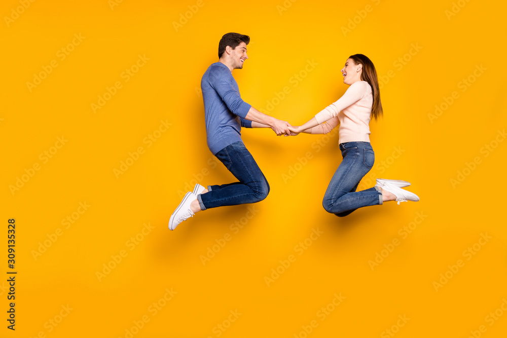 Full body profile side photo of funky two students married people jump relax rest hold hand feel rejoice emotions wear blue pink outfit sneakers isolated over yellow color background