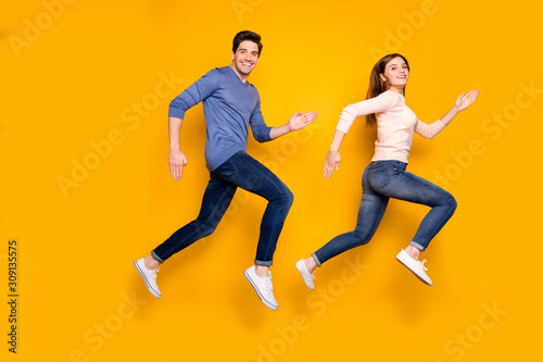 Full size profile side photo of funky two married people jump run after summer black friday bargains wear blue pink pullover denim jeans sneakers isolated over bright color background