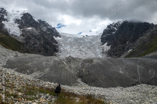 Man tourist going to huge Lardaad glacier and its moraine through boulders stones and grass while hiking in mountains photo