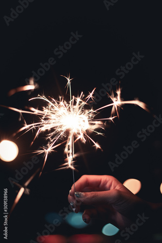 Woman's hand holding sparklers stick on fire, big flame spread long light with bokeh of light bulb at night time on black background