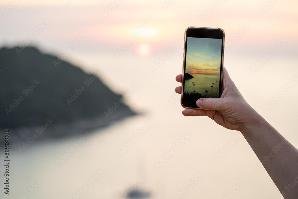 Woman's hand with smartphone makes photo of sunset at sea.