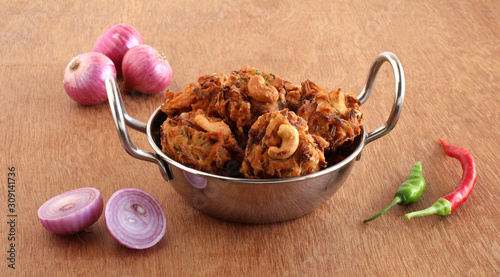 Pakoda, or pakora, a traditional, popular, and vegetarian Indian snack and side dish, with onion as the main ingredient, in a steel wok on a wooden background.
