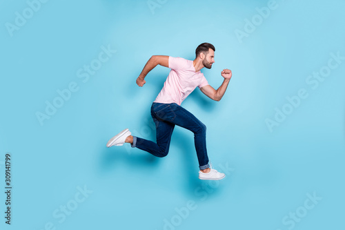 Full length profile photo of attractive guy jumping high sportive competitions participant wear casual pink t-shirt jeans sneakers isolated blue color background