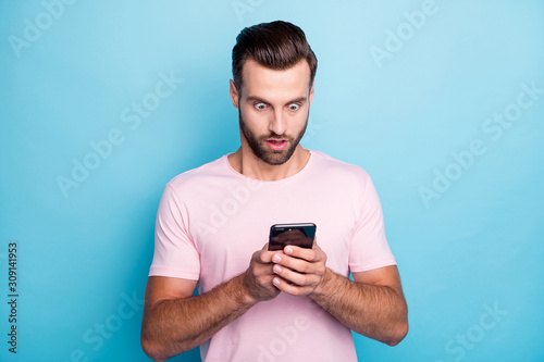 Photo of attractive guy holding telephone hands open mouth reading bad news negative post comments followers wear casual pink t-shirt isolated blue color background © deagreez