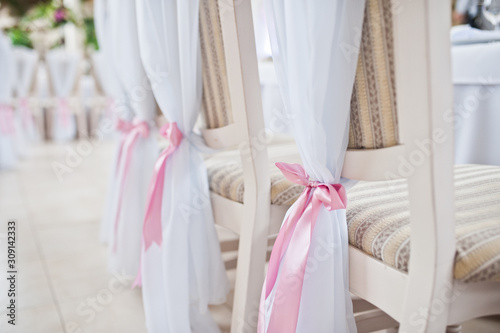 Beautiful wedding set decoration in the restaurant. Pink ribbons on chairs.