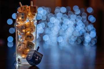 jewish holiday Chanukah/Hanukkah with wooden dreidels / sovivon (spinning top) in the glass over glitter shiny background. Traditional invitation card design