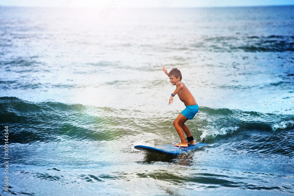 Little boy balancing on the surf board in sea