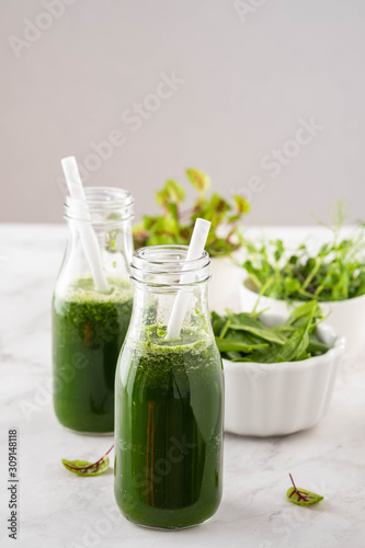 Blended green smoothie with ingredients on the white table.