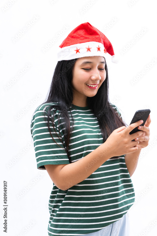 portrait of a young Asian woman wearing a santa hat and wearing casual clothes using a smartphone portrait of a young Asian woman wearing a santa hat and wearing casual clothes using a smartphone