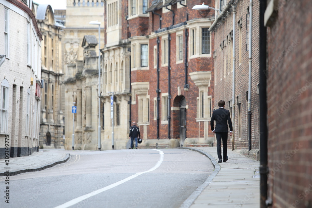 A man walking down a srtreet on a September day in Cambridge, England