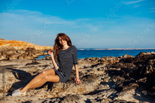 girl sits on the rocky beach enjoys sunshine