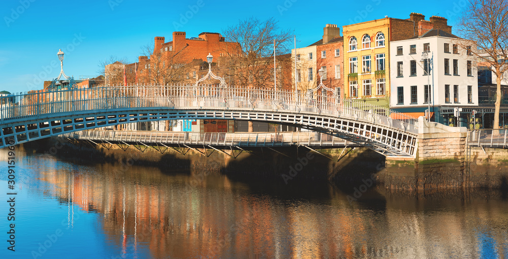 Fototapeta premium Dublin, panoramic image of Half penny bridge, or Ha'penny bridge, on a bright day with beautiful reflection of historic houses and pubs of the riverside in river Liffey