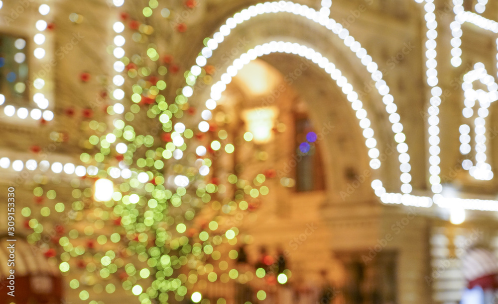 The building is decorated with electric garlands. Light colored spots on the facade. Festive background, blurred image.