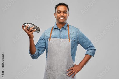 alcohol drinks, people and profession concept - indian barman in apron with cocktail shaker over grey background photo