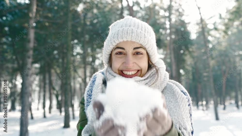 Closeup portrait of funny smiling woman in wooly hat and long warm scarf holding snow in hands to the camera snowy winter park in frozzy sunny day. Happy winter time, having fun slow motion Closeup portrait of funny smiling woman in wooly hat and long warm scarf holding snow in hands to the camera snowy winter park in frozzy sunny day. Happy winter time, having fun slow motion