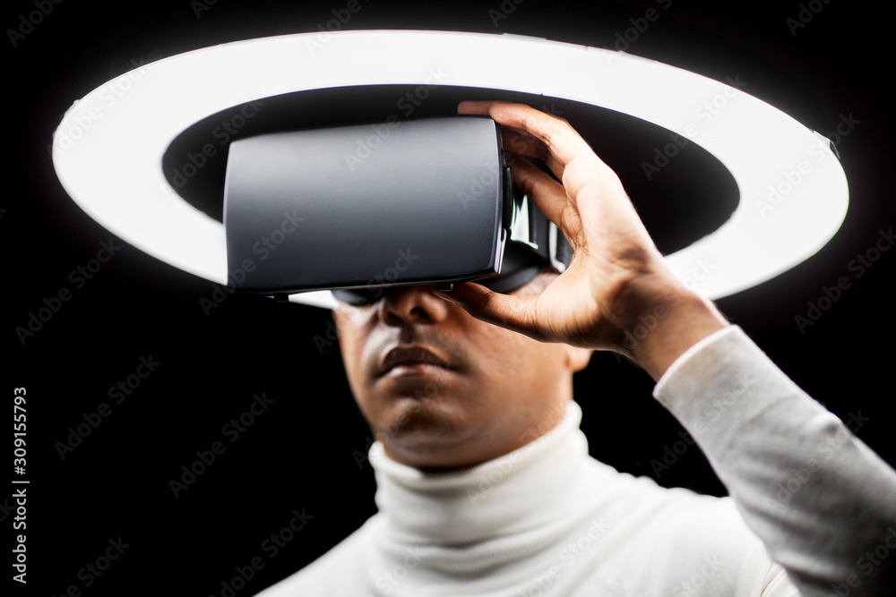 future technology, augmented reality and people concept - man in virtual reality headset or vr glasses under white illumination over black background