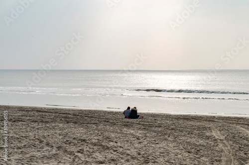 Solitude people relax chill out on the lonely beach in the cold season. Sea winter holidays. Gray seascape at sunset on the North Sea with sun glare on the water.