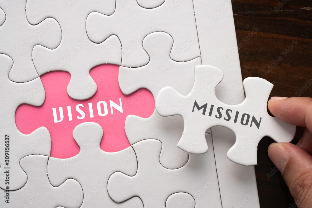 Fototapeta premium Hand hold piece of puzzle written MISSION revealing word VISION Business concept.