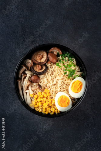 Ramen noodle soup. Soba noodles with eggs, shiitake and enoki mushrooms, corn and scallions, overhead shot on a black background with copy space