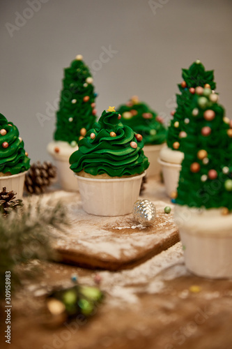 Selective focus of decorated Christmas tree cupcakes with sweet cream and spruce cones on table