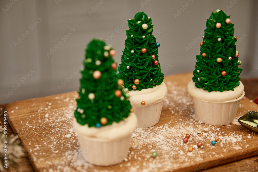 Selective focus of Christmas tree cupcakes with flour and christmas ball on cutting board Selective focus of Christmas tree cupcakes with flour and christmas ball on cutting board