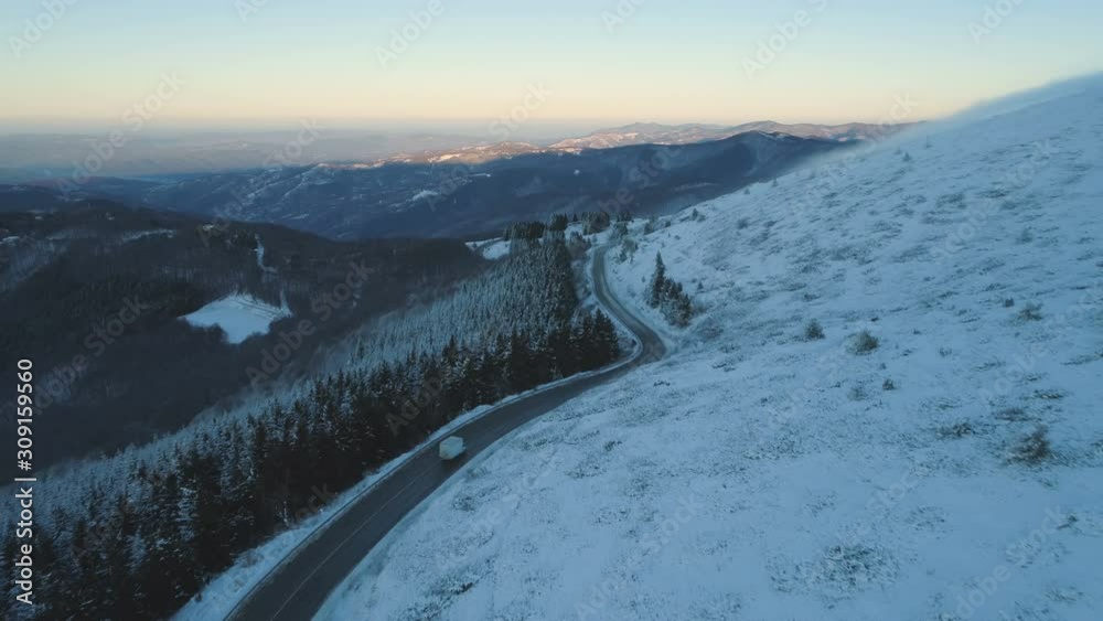 Drone chasing car or truck on mountain road at susnet during winter