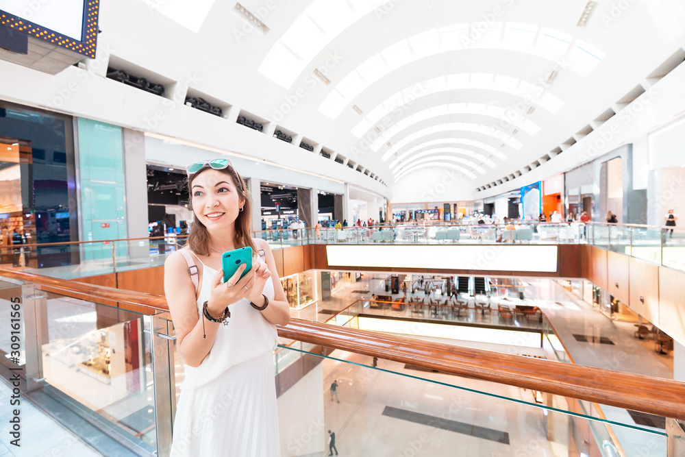 Fototapeta premium Happy Asian girl gets a marketing newsletter with discounts on her smartphone. Profitable modern shopping in the interior of the shopping center