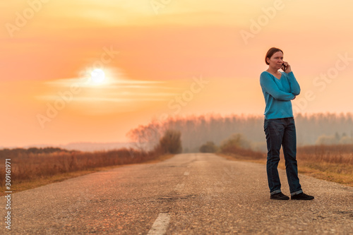 Woman standing on countryside road and talking on mobile phone
