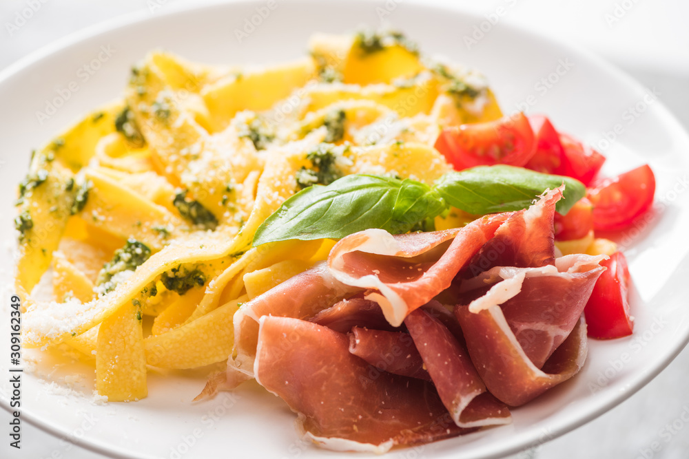 close up view of delicious Pappardelle with tomatoes, Parmesan, pesto sauce, basil and prosciutto close up view of delicious Pappardelle with tomatoes, Parmesan, pesto sauce, basil and prosciutto