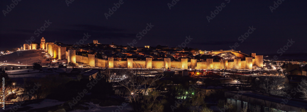 Ávila y su muralla con nieve iluminado al anochecer (España).