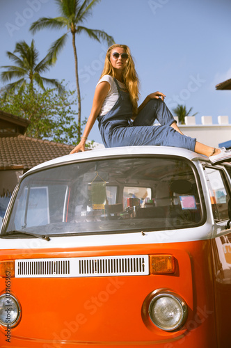 Beautiful blonde girl in modern fashion on a background of palm trees, a hippie car. Dissolute girl with happy emotions.