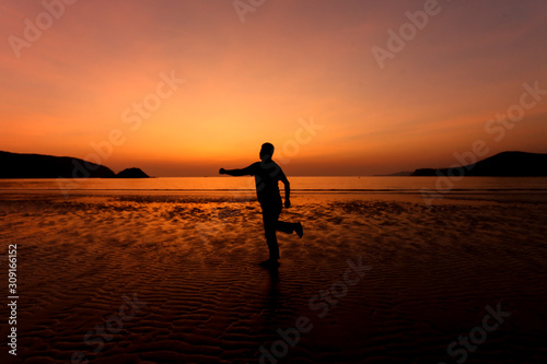 Silhouette action of a young man fun under twilight sunset sky at sea beach.