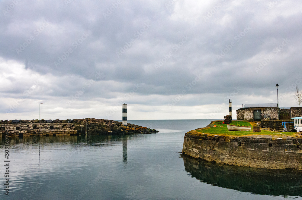 Small harbor in fishing village of Carnlough of Northern Ireland under cloudy skies with a view of sea beyond. Small harbor in fishing village of Carnlough of Northern Ireland under cloudy skies with a view of sea beyond.