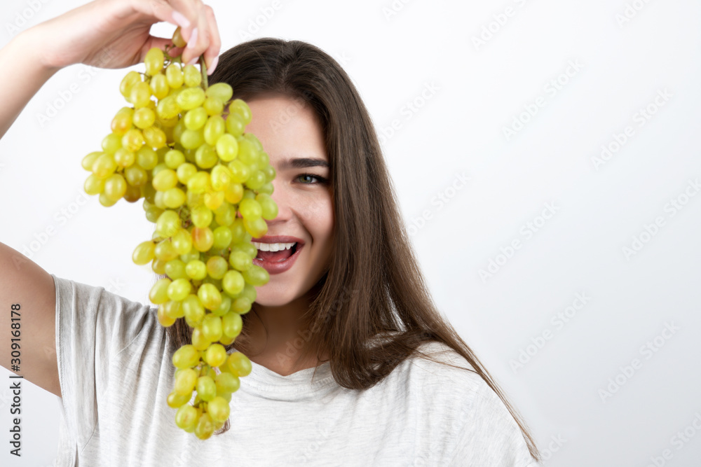young beautiful woman holding bunch of green grapes near her face looking seductive standing on isolated white background dietology and nutrition young beautiful woman holding bunch of green grapes near her face looking seductive standing on isolated white background dietology and nutrition