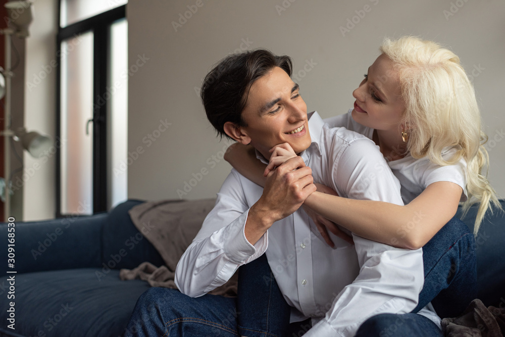 Smiling young couple hugging and holding hands on sofa in living room
