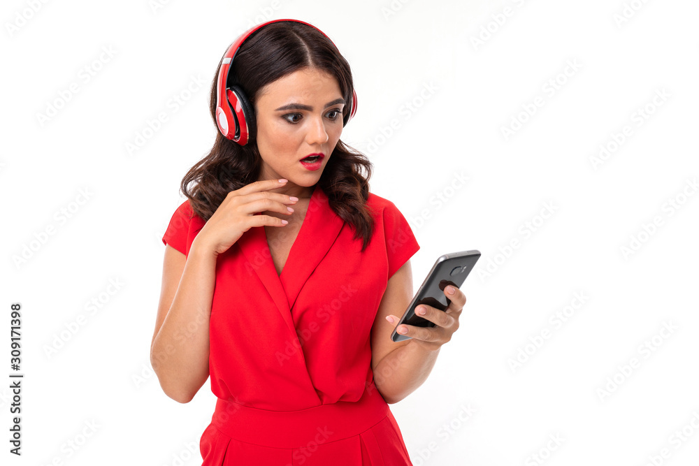 attractive brunette girl in a red dress in headphones with a telephone on a white wall attractive brunette girl in a red dress in headphones with a telephone on a white wall