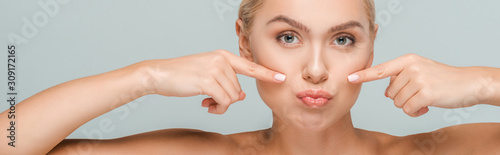 panoramic shot of naked woman pointing with fingers at clean face isolated on grey