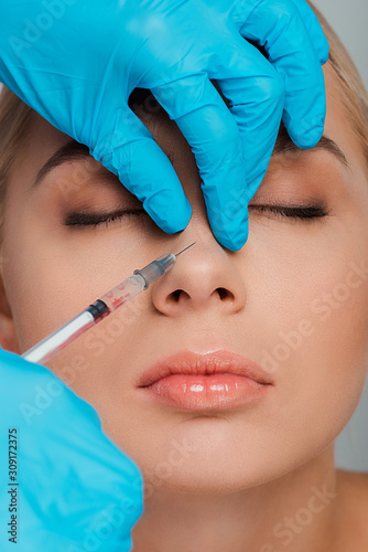 cropped view of beautician in latex gloves holding syringe near nose of girl with closed eyes