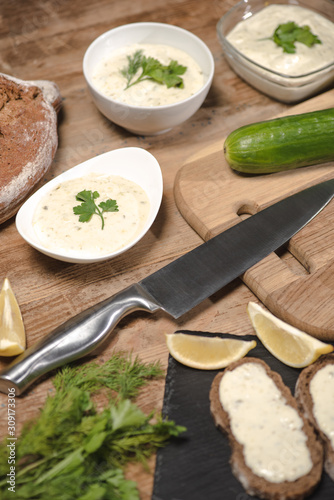 Tasty homemade tzatziki sauce with bread and greenery on wooden table