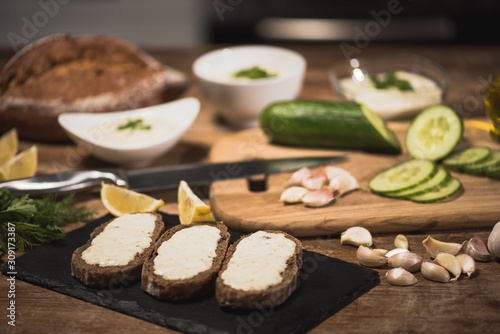 Selective focus of bread with tzatziki sauce and fresh ingredients on wooden table